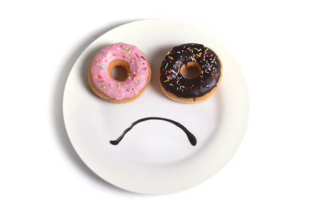 40416419 - smiley sad face worried about overweight made on dish with donuts as eyes and chocolate syrup as mouth in sugar and sweet addiction , diet and nutrition concept isolated on white background
